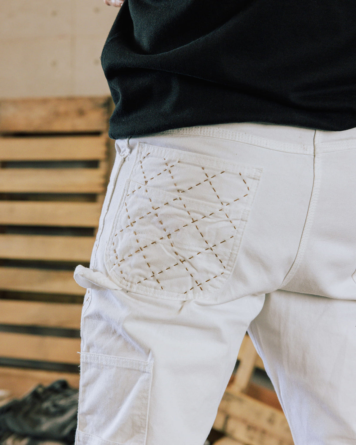 White work pants with brown crisscross stitching on the back pocket and a hammer loop, worn with a black top.