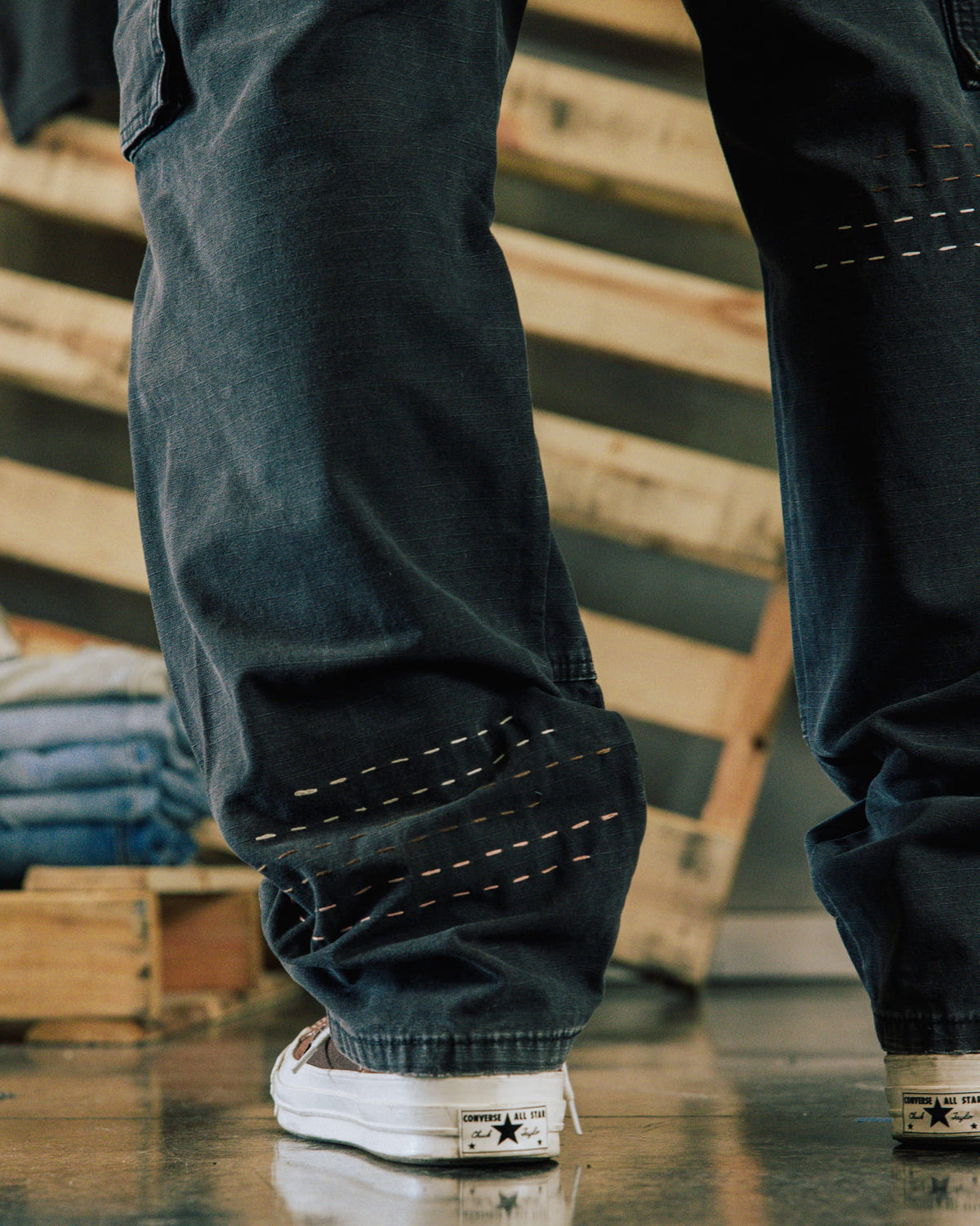Dark blue wide-leg denim pants with contrast running stitches, worn with white sneakers on a polished floor.