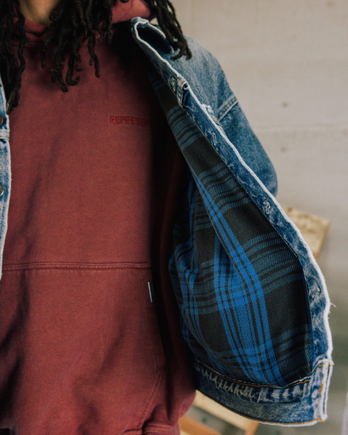 Person wearing a burgundy hoodie under an open blue denim jacket with blue and black plaid lining.