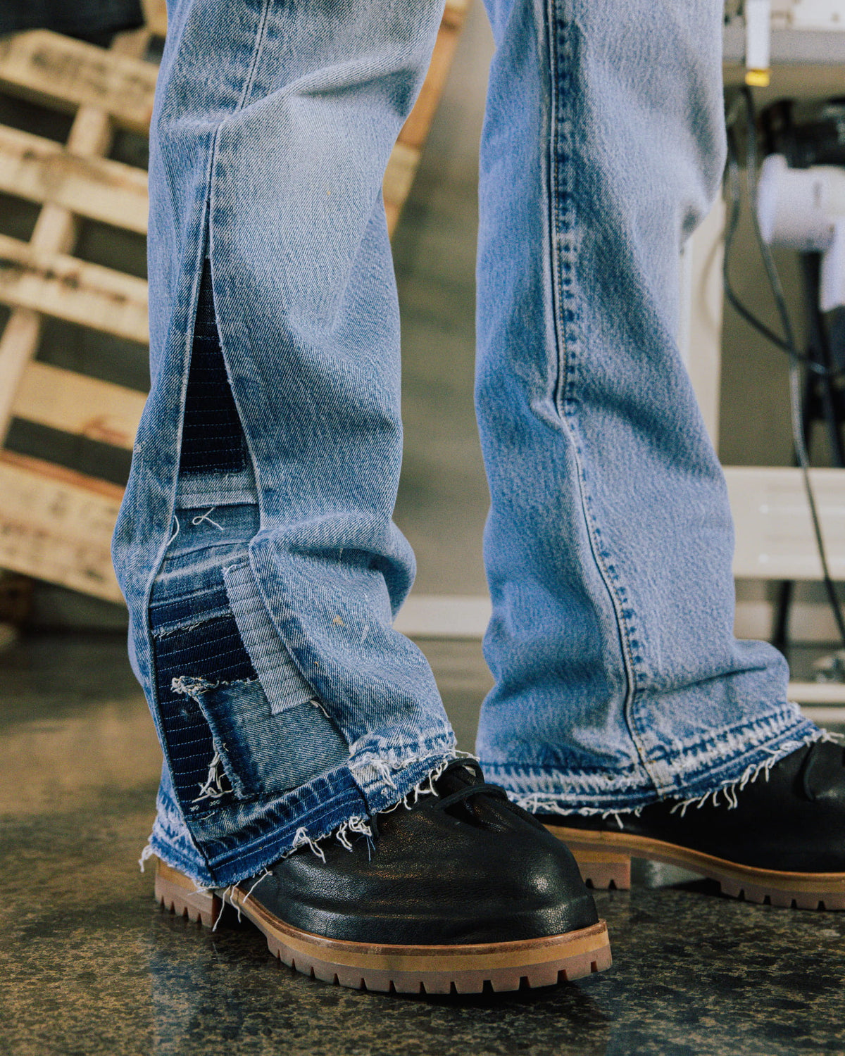 Light blue patchwork denim jeans with frayed hems worn over black leather lace-up shoes with tan lug soles.