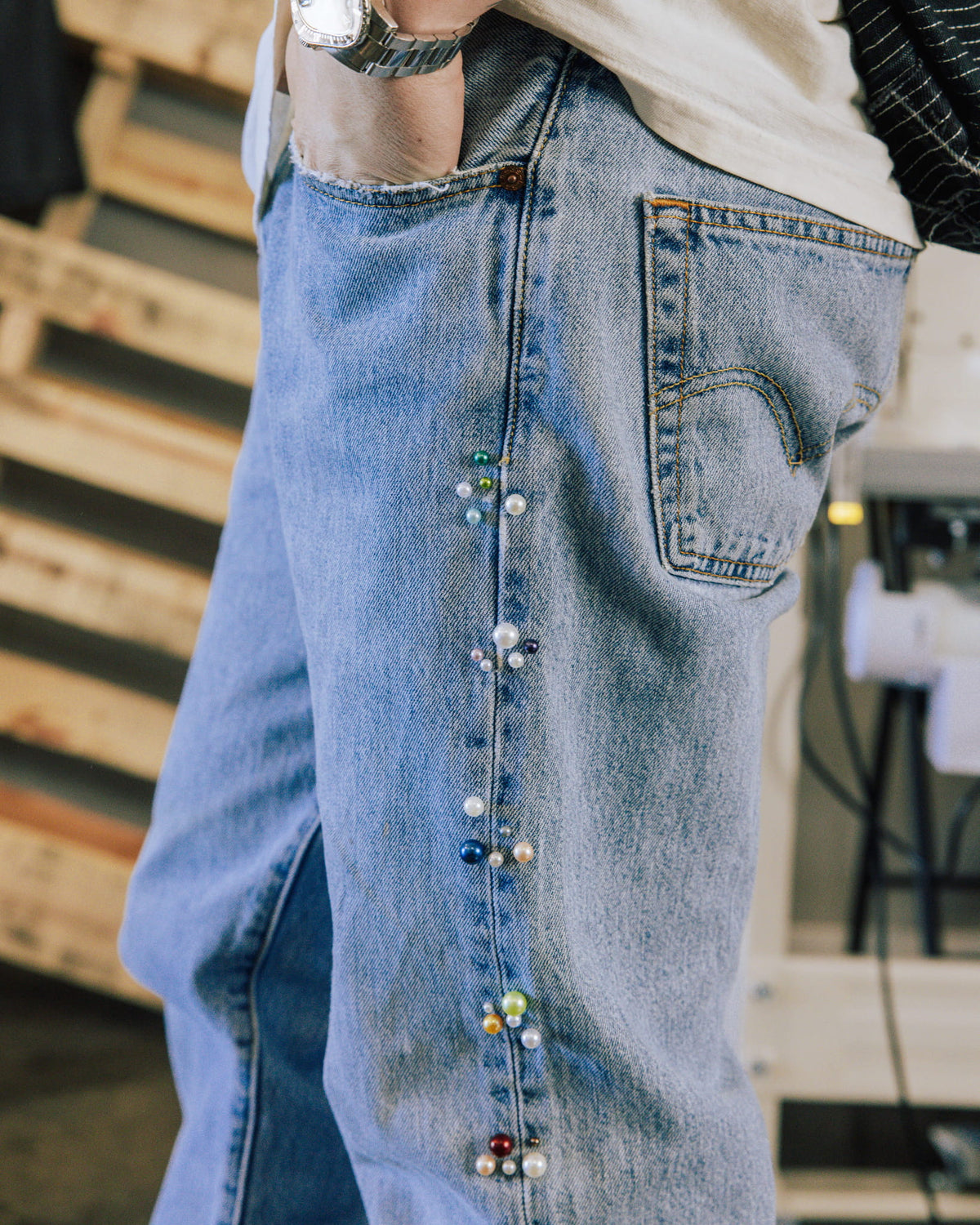 Light blue denim jeans with multicolored pearl-like beads along the side seam, worn with a white top and silver watch.