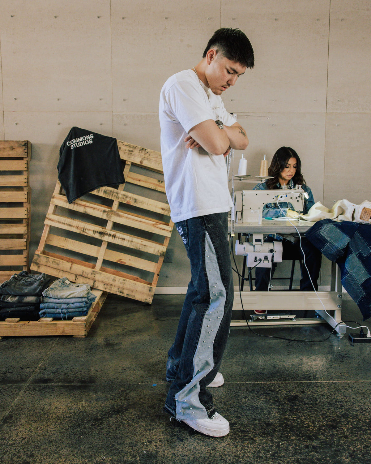Man wearing a white T-shirt and dark denim jeans with studded light blue side panels in a sewing studio.