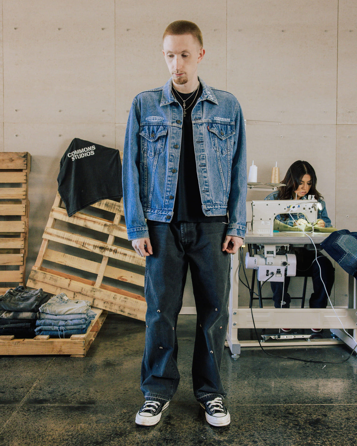Man wearing a blue denim jacket with white embroidery and dark jeans in a sewing workshop.