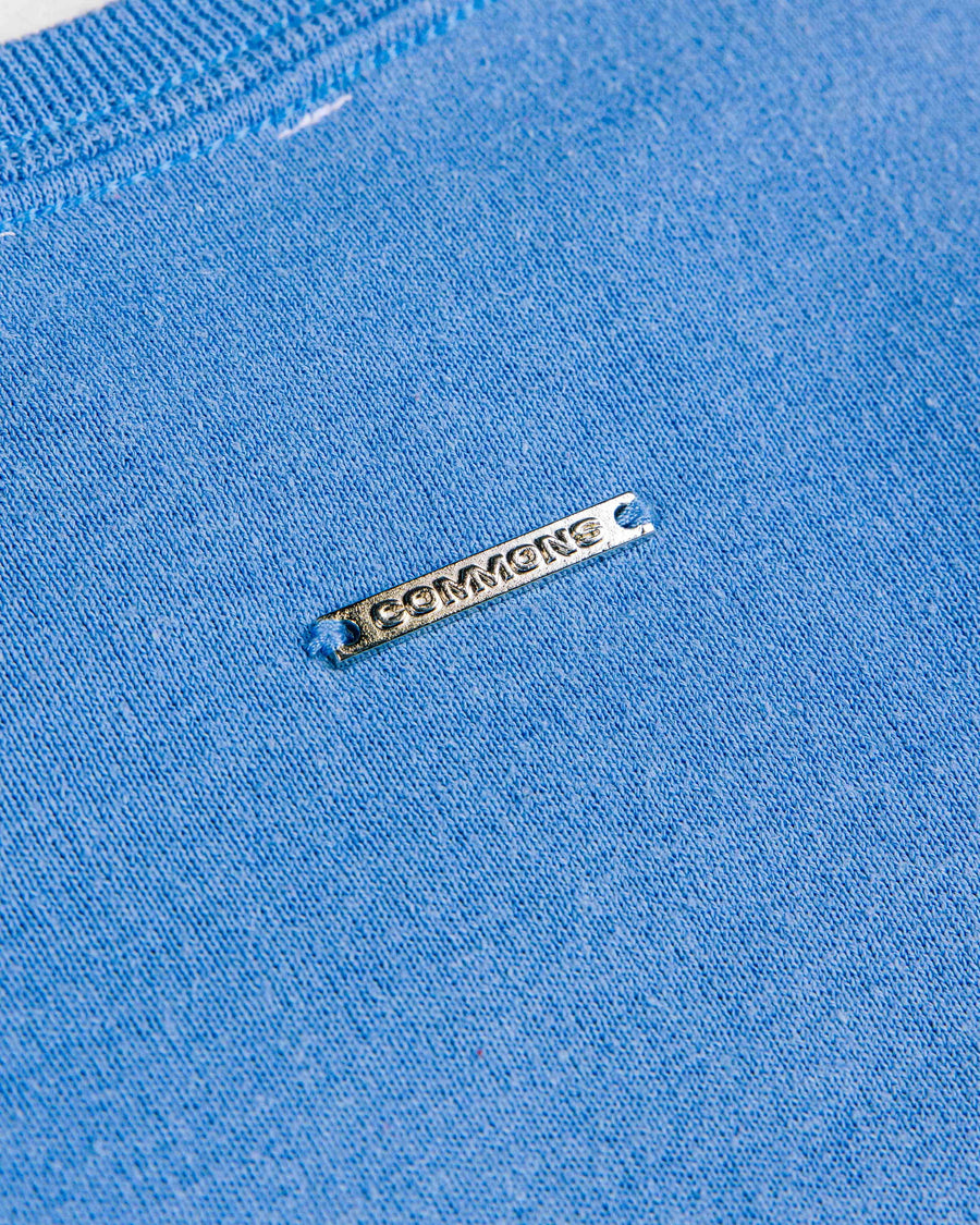 Close-up of a blue knit garment with ribbed trim and a silver-tone COMYONG metal tag.