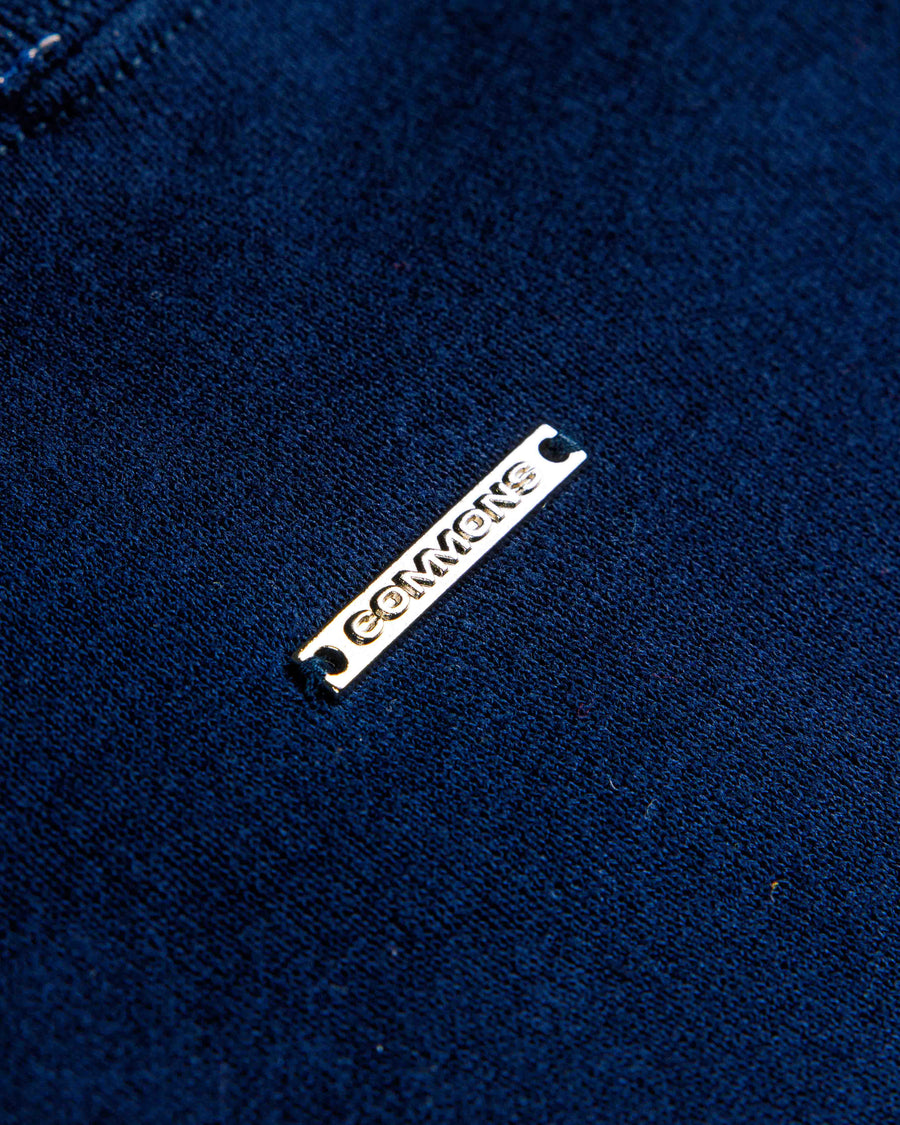 Close-up of navy blue knit fabric with a slim silver-tone metal logo tag stitched in place.