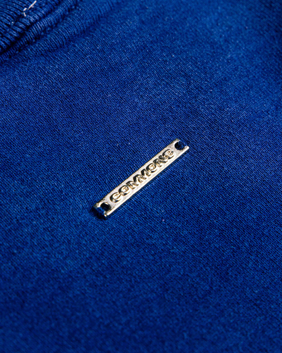 Close-up of royal blue knit fabric with a silver-tone rectangular logo tag and stitched seam.