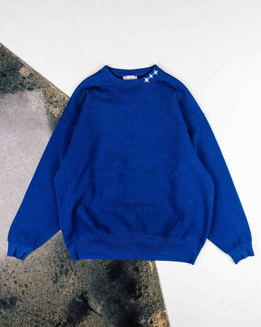 Royal blue crewneck sweatshirt with three white stars on the collar and ribbed cuffs and hem, laid flat.