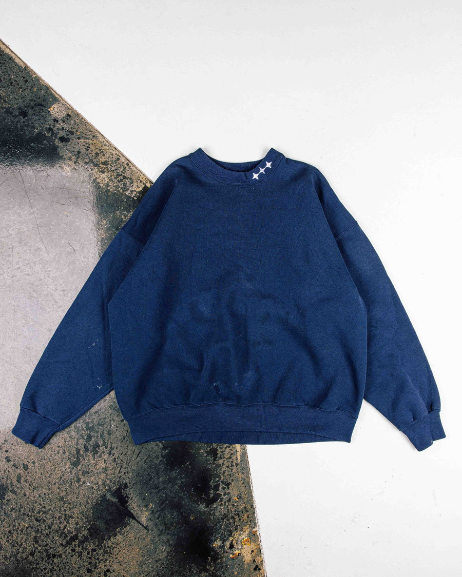 Navy blue crewneck sweatshirt with three white stars at the collar and ribbed cuffs, laid flat on a worn floor.