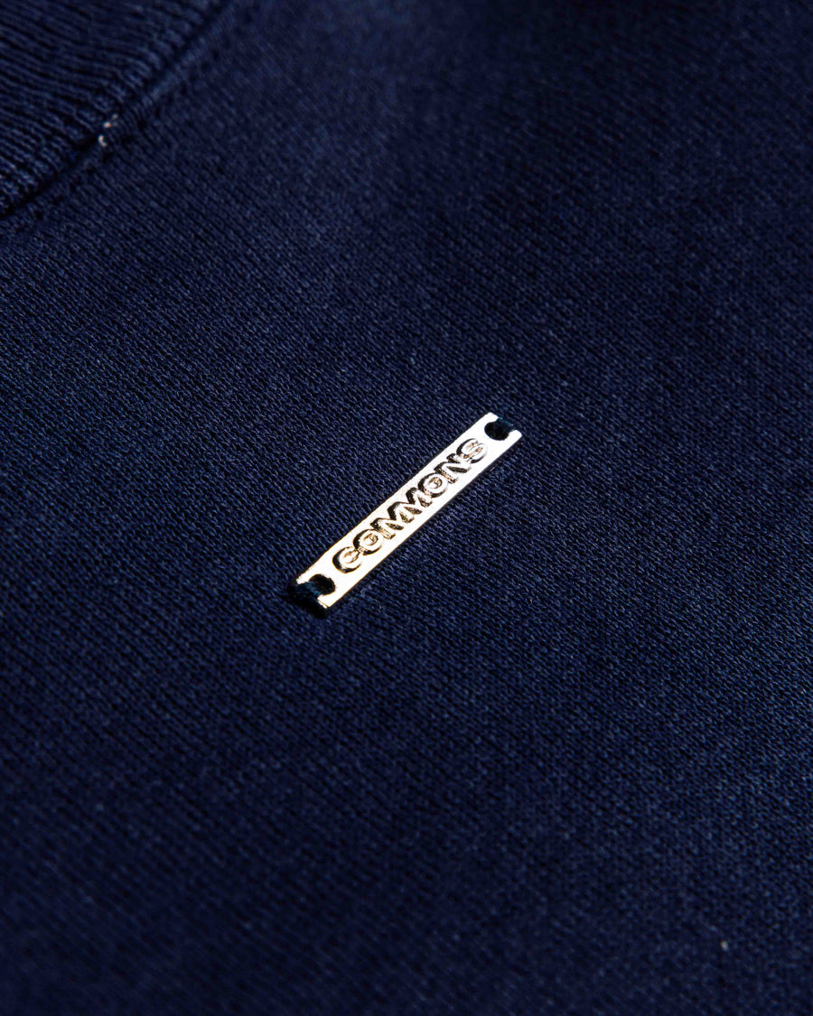 Close-up of a navy blue knit garment with a ribbed neckline and a small rectangular metal logo tag.