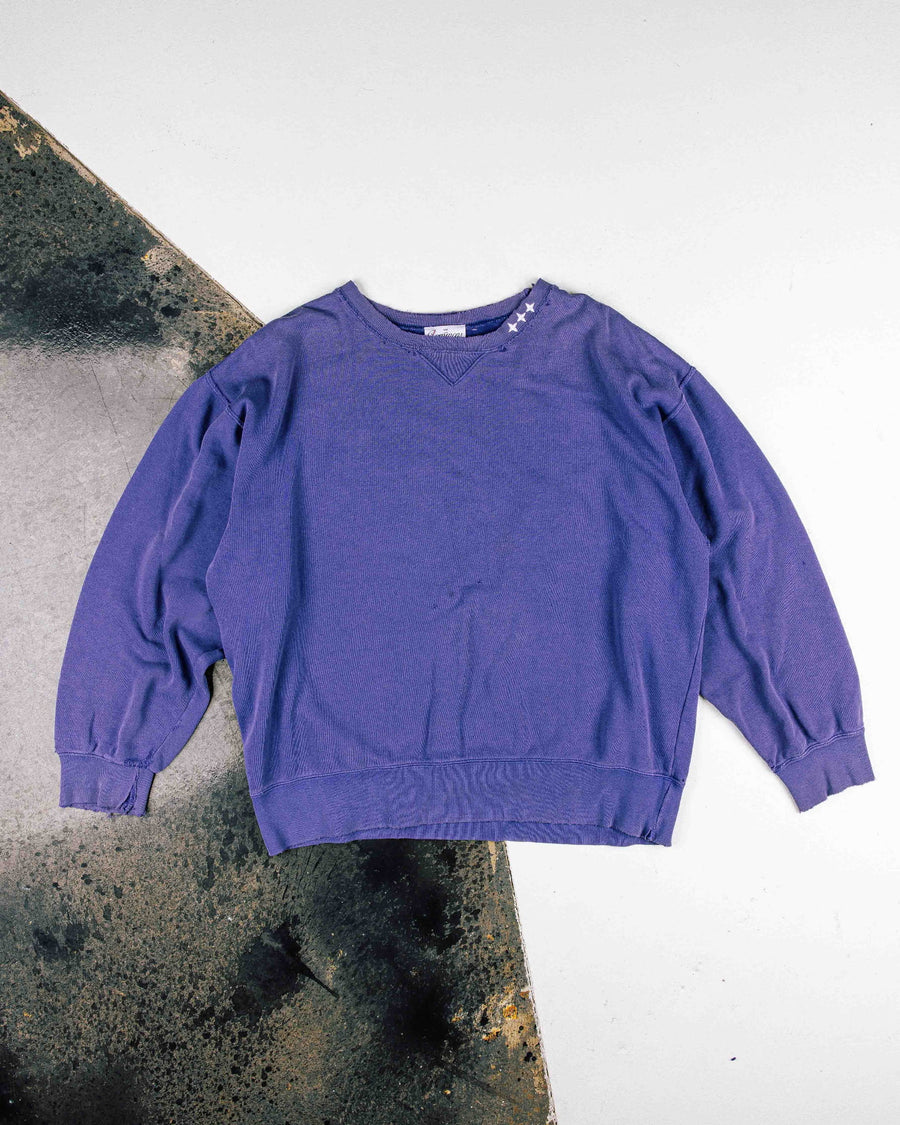 Purple crewneck sweatshirt with white stars at the collar and ribbed cuffs, laid flat on a white and weathered surface.