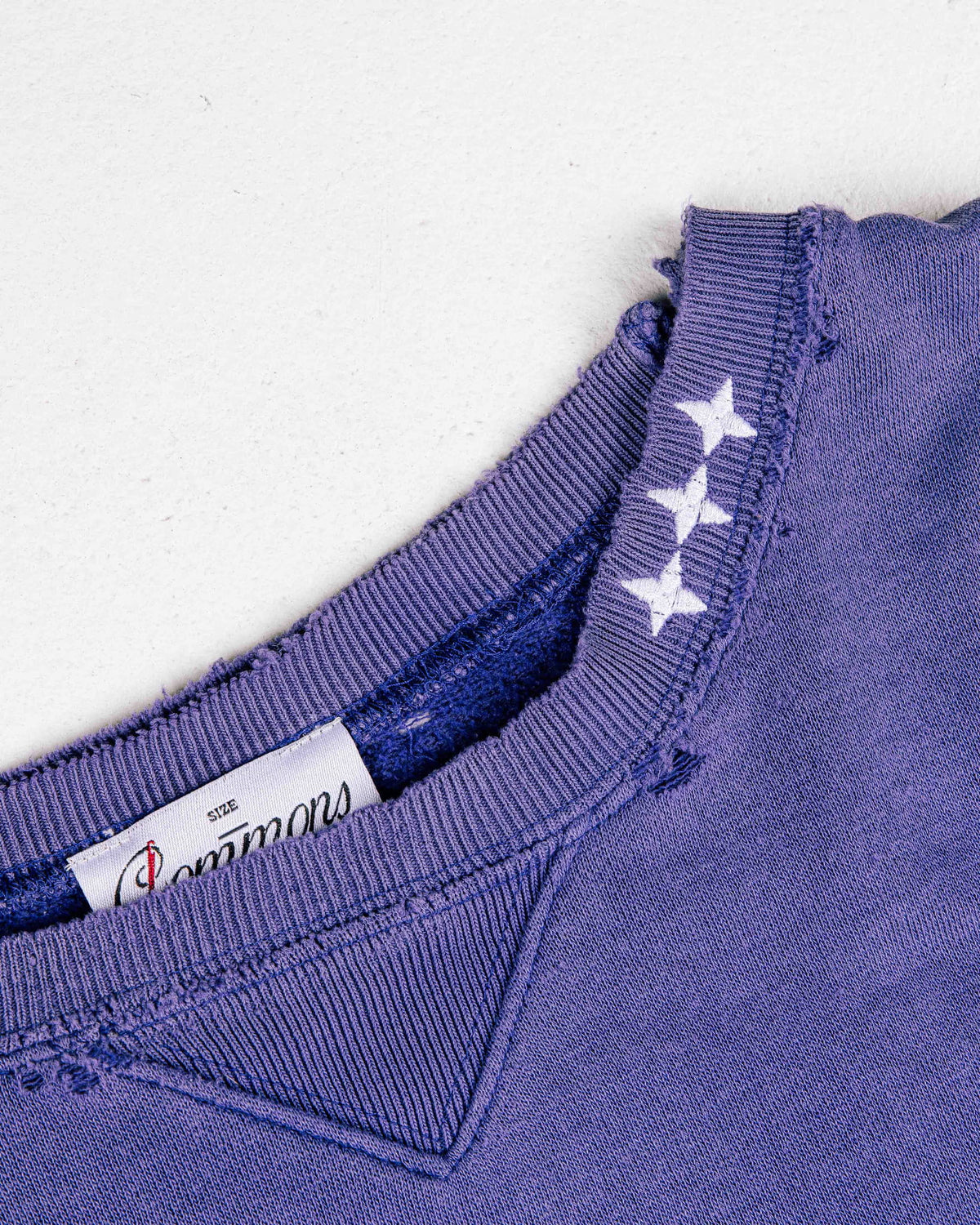 Close-up of a purple sweatshirt with a distressed ribbed neckline, three white stars, and a triangular inset.