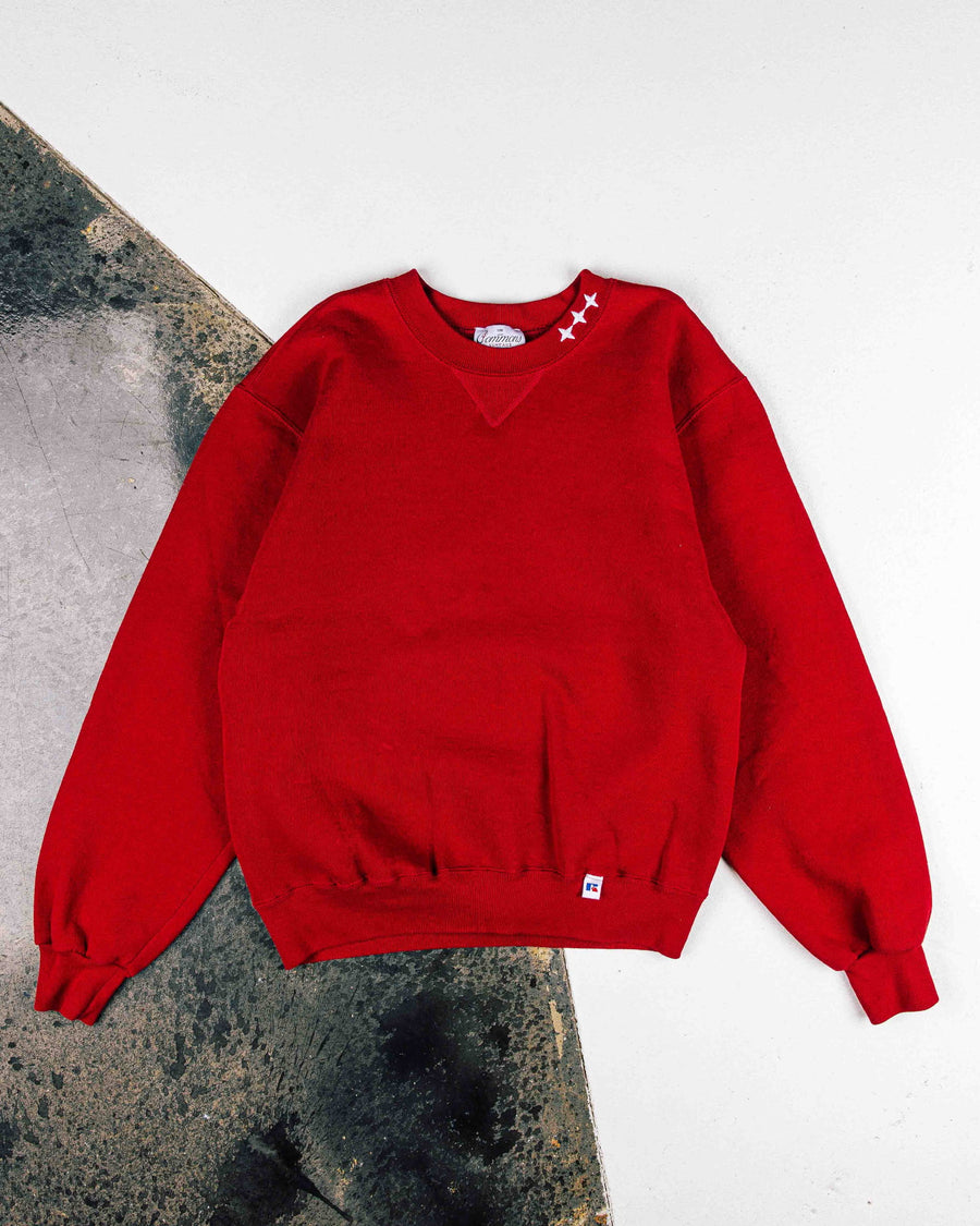 Red crewneck sweatshirt with white stars at the collar and ribbed cuffs and hem, laid flat on a white and gray surface.