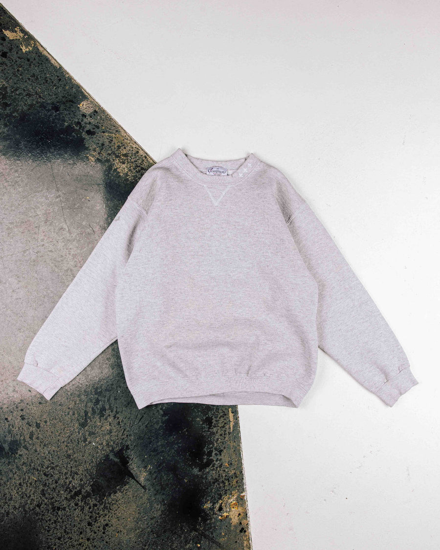 Light gray heather crewneck sweatshirt with long sleeves and ribbed trim, laid flat on a white and weathered dark surface.
