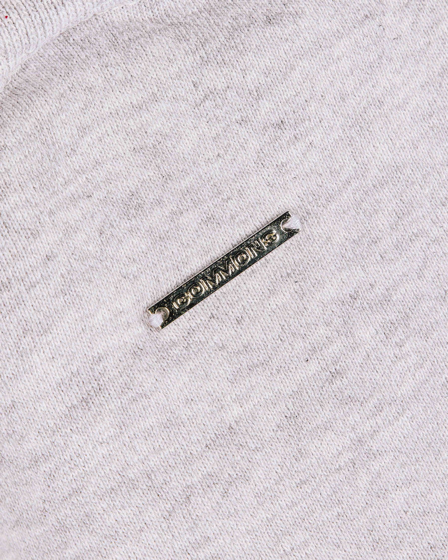 Close-up of light gray knit fabric with a rectangular silver-tone metal logo tag stitched in place.