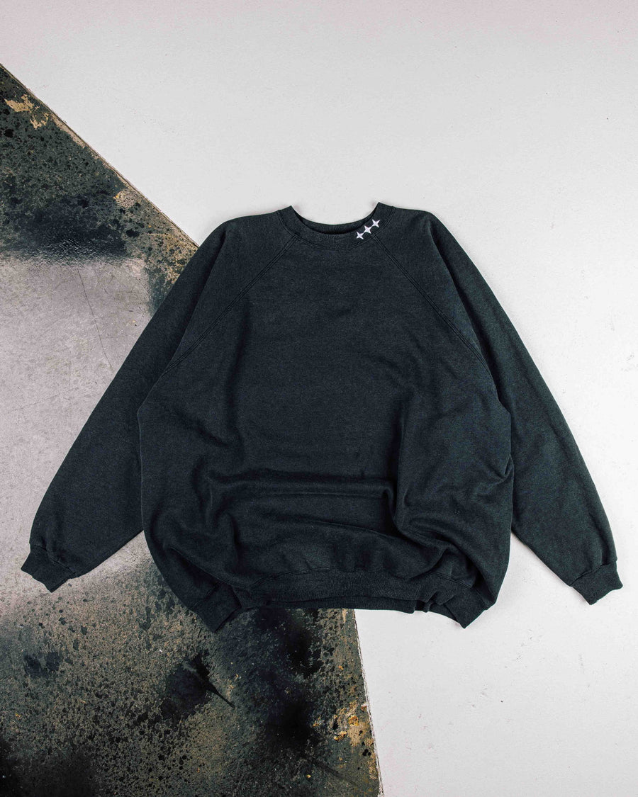 Charcoal crewneck sweatshirt with raglan sleeves and three white stars at the collar, laid flat on a two-tone floor.