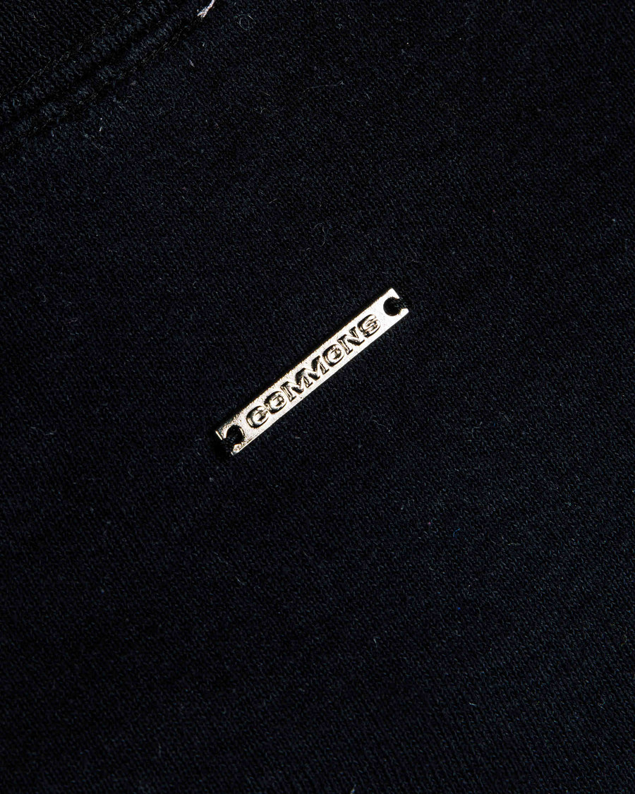 Close-up of black knit fabric with a stitched seam and a silver-tone metal logo tag.