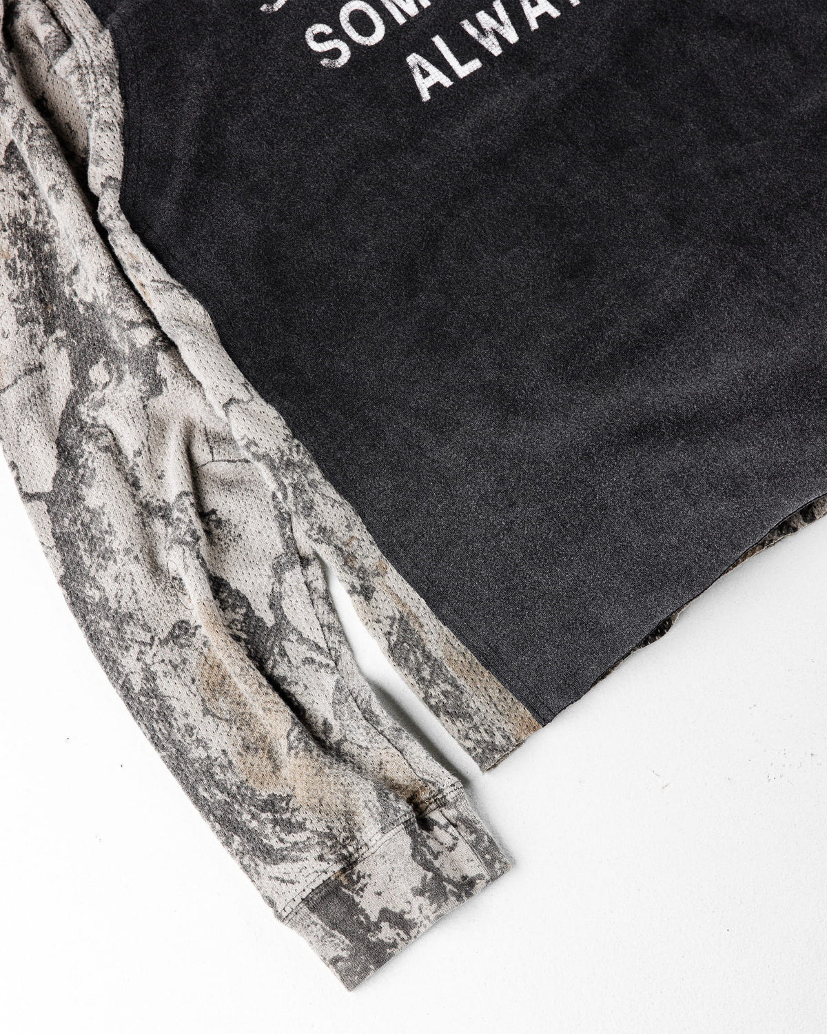 Close-up of a charcoal top with white lettering and gray camouflage long sleeves on a white surface.