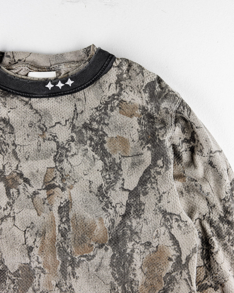 Gray and brown camouflage mesh shirt with a black ribbed collar and three white stars, laid on a white surface.