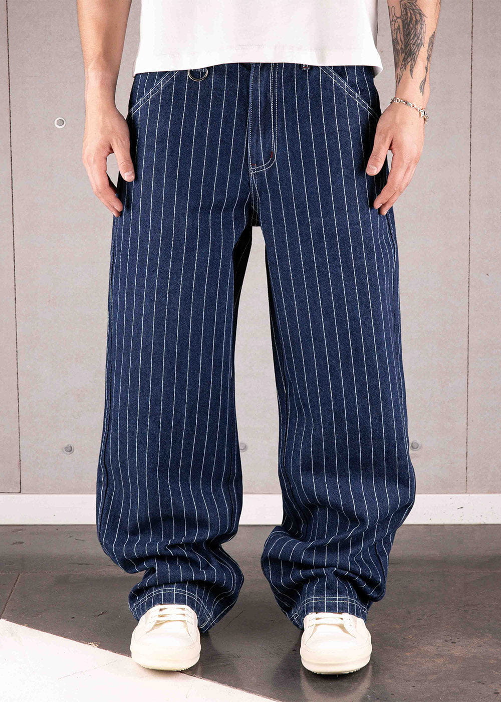 Model wearing loose navy pinstriped denim pants with contrast stitching, a white T-shirt, and white sneakers.