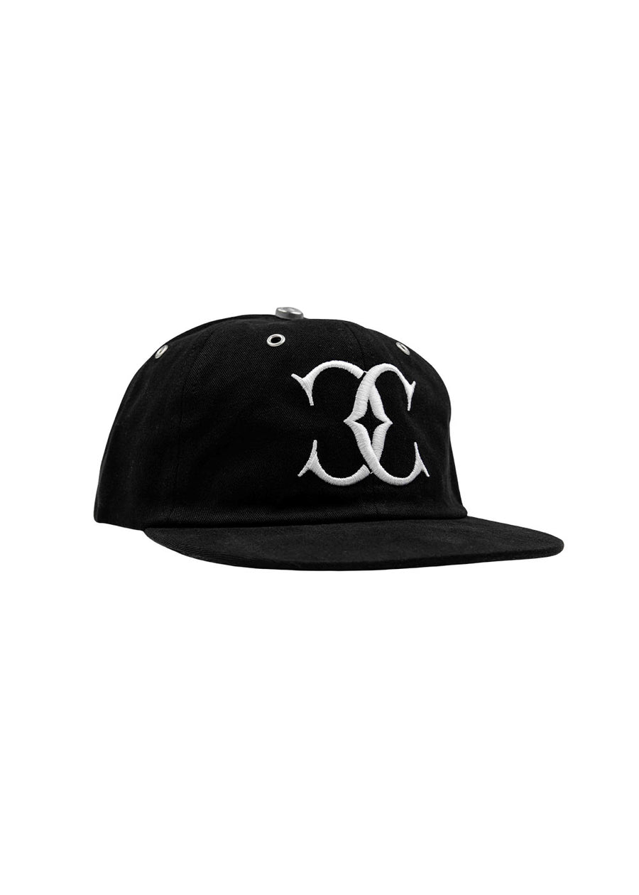 Black fabric flat-brim cap with a white embroidered front logo and silver-tone eyelets on a white background.