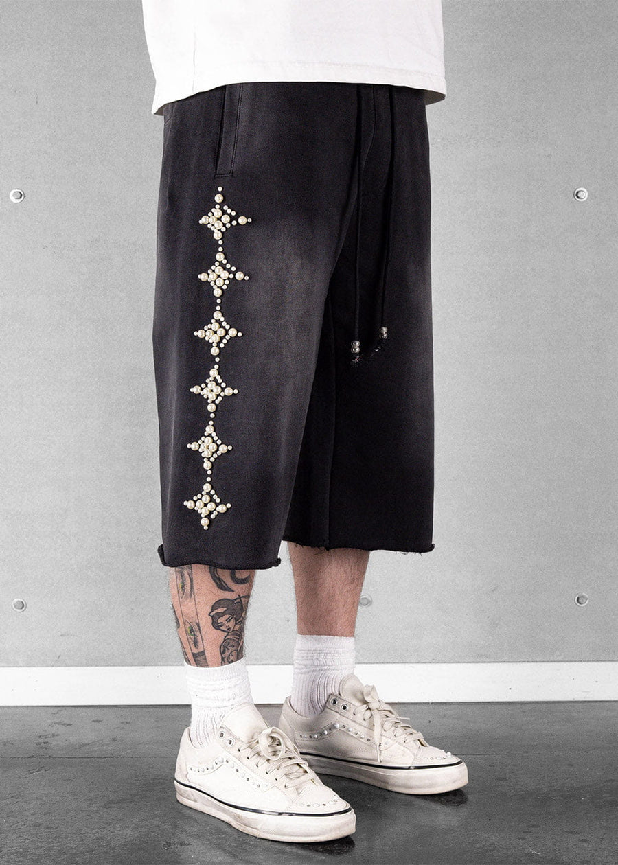 Black knee-length drawstring shorts with pearl-like diamond embellishments, worn with a white shirt and cream sneakers.