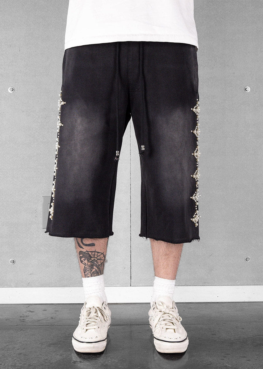 Black wide-leg drawstring shorts with pearl side embellishments and raw hems, worn with a white shirt and cream sneakers.