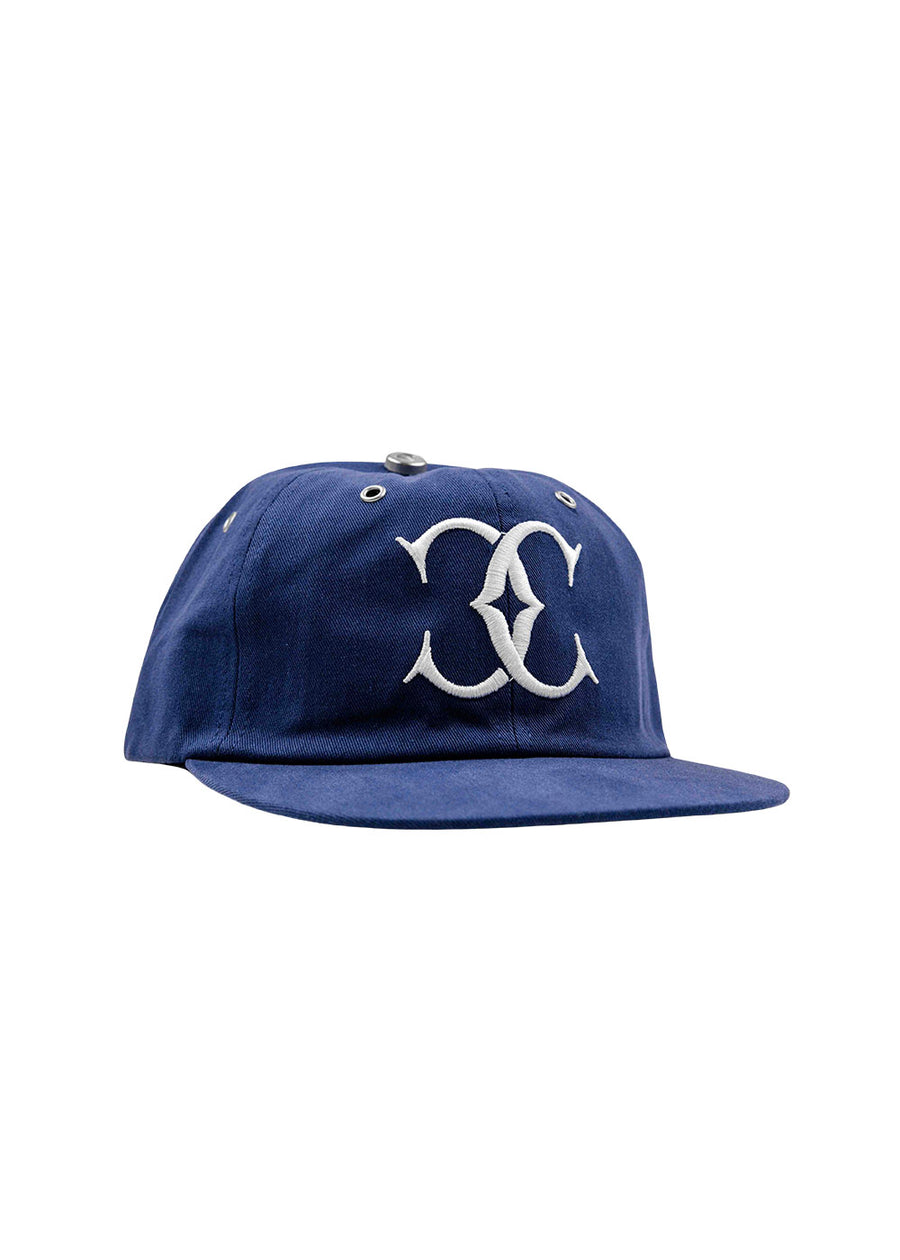 Blue fabric baseball cap with a flat brim, white embroidered emblem, and silver metal eyelets on a white background.