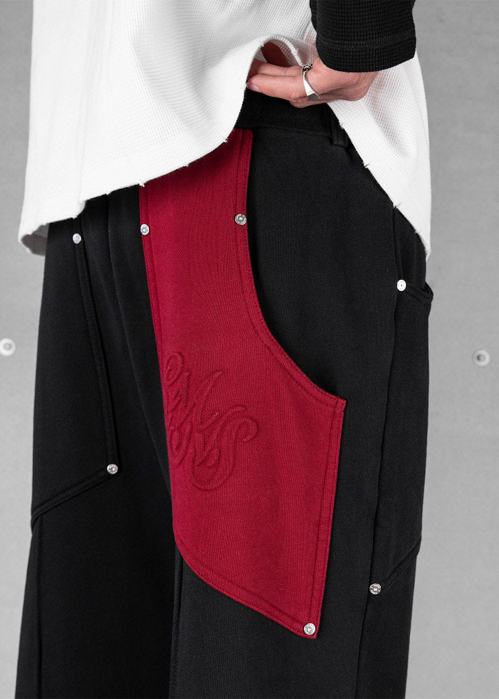 Close-up of black knit sweatpants with a red side panel, tonal embroidery and silver studs, worn with a white top.