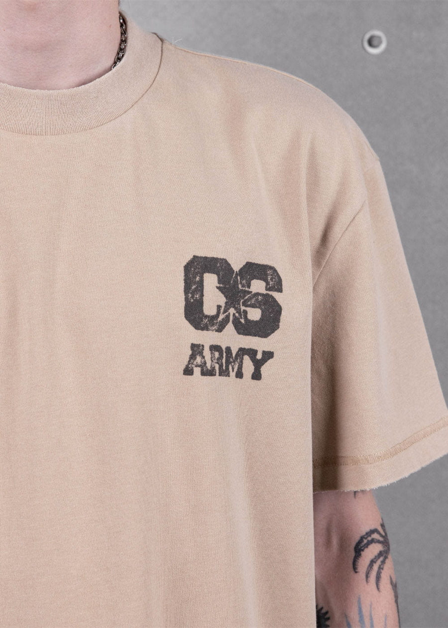 Person wearing a beige crewneck T-shirt with a distressed black star and ARMY chest print against a gray wall.