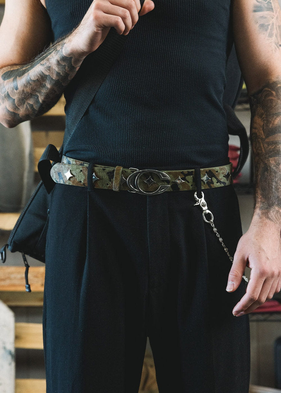 Camouflage belt with silver-tone star studs and an oval buckle, worn with black trousers and a black ribbed top.