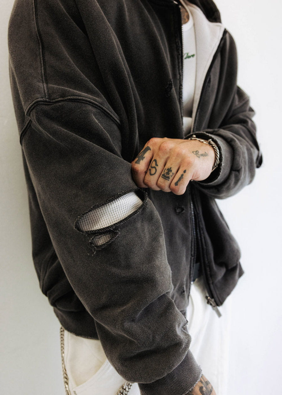 Person wearing a faded black zip-up hoodie with distressed sleeves exposing white waffle-knit lining and ribbed cuffs.