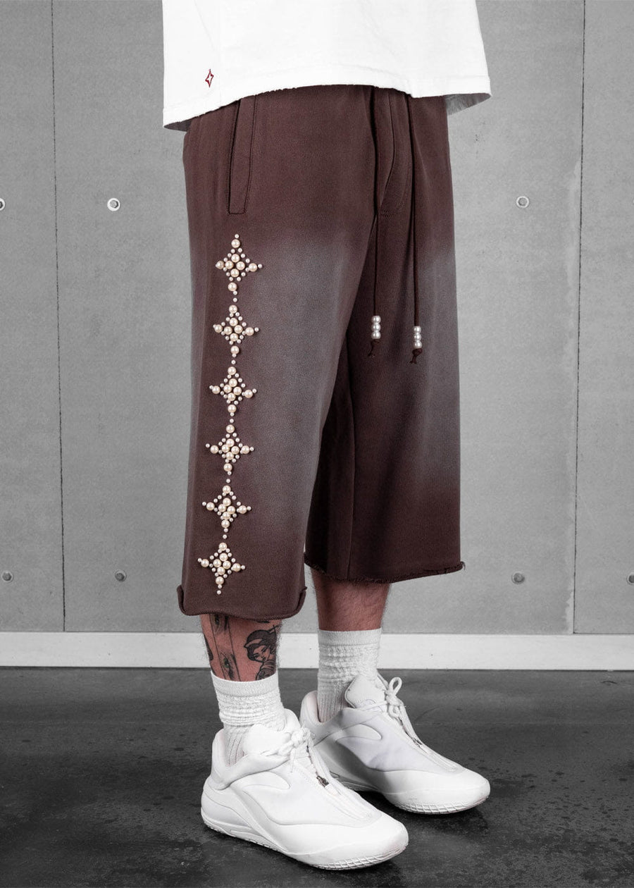 Brown wide-leg cropped pants with pearl diamond motifs and beaded drawstrings, worn with a white tee and sneakers.