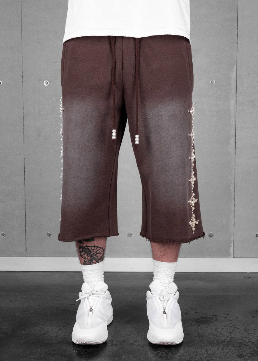 Brown wide-leg cropped pants with faded thighs, raw hems and pearl-beaded sides and drawstrings, worn with white sneakers.