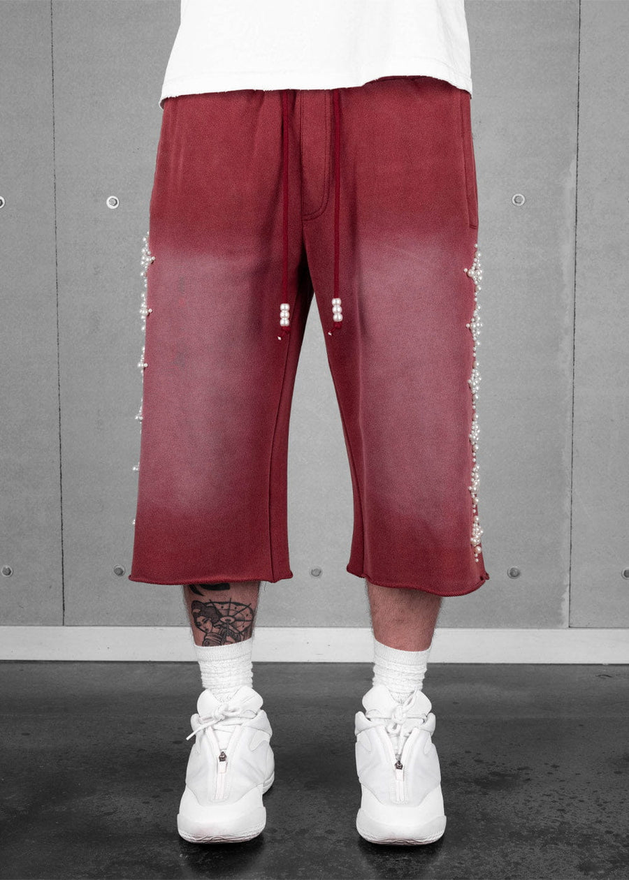 Burgundy wide-leg cropped pants with faded thighs, pearl-like side beads and drawstring tips, worn with white sneakers.