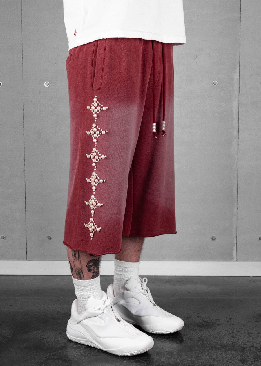 Burgundy long shorts with pearl-like star embellishments and beaded drawstrings, worn with a white T-shirt and sneakers.