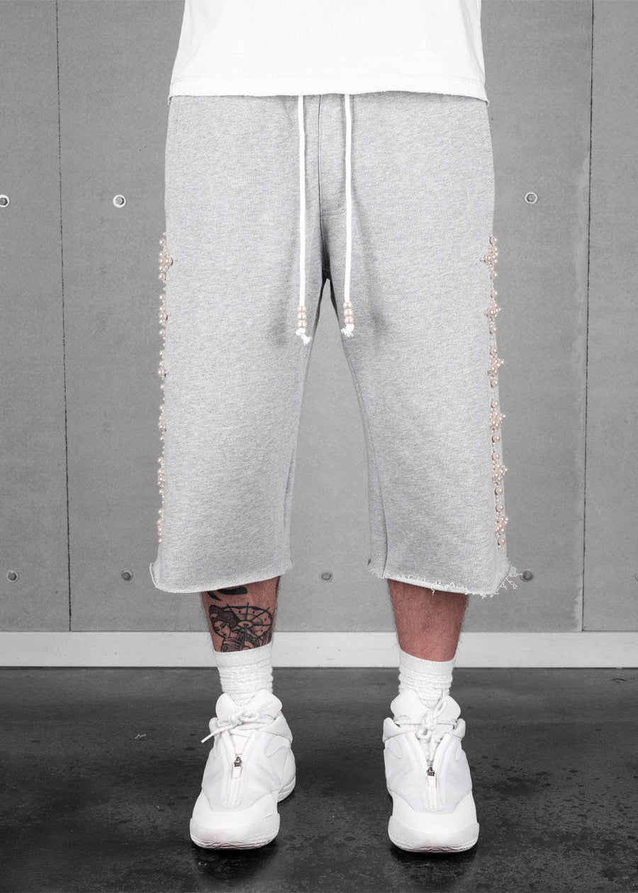 Model wearing light gray knit cropped pants with raw hems, pearl-like side beads, white drawstrings, and white sneakers.