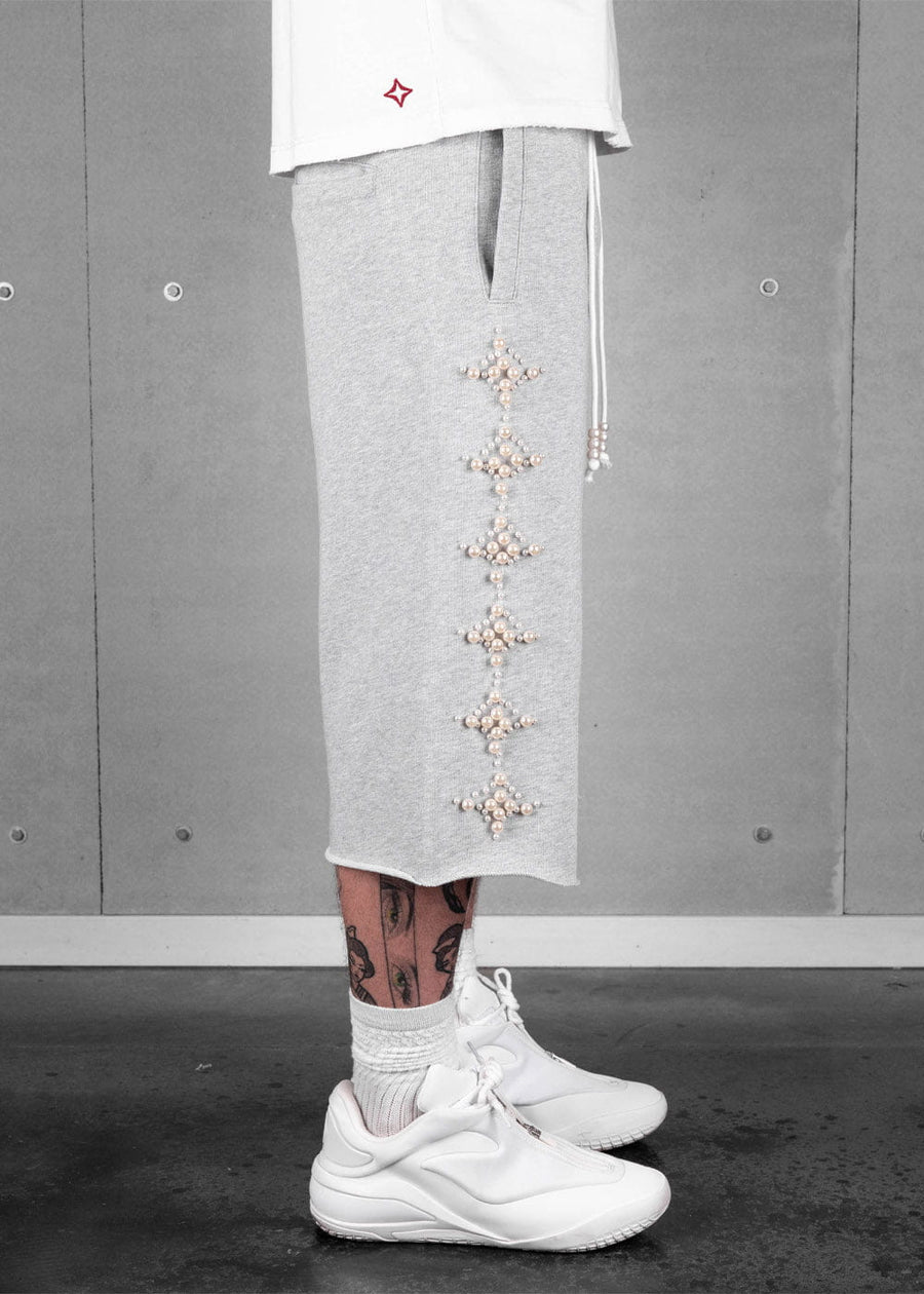 Model wearing heather gray long shorts with pearl-like star embellishments, a side pocket, and white sneakers.