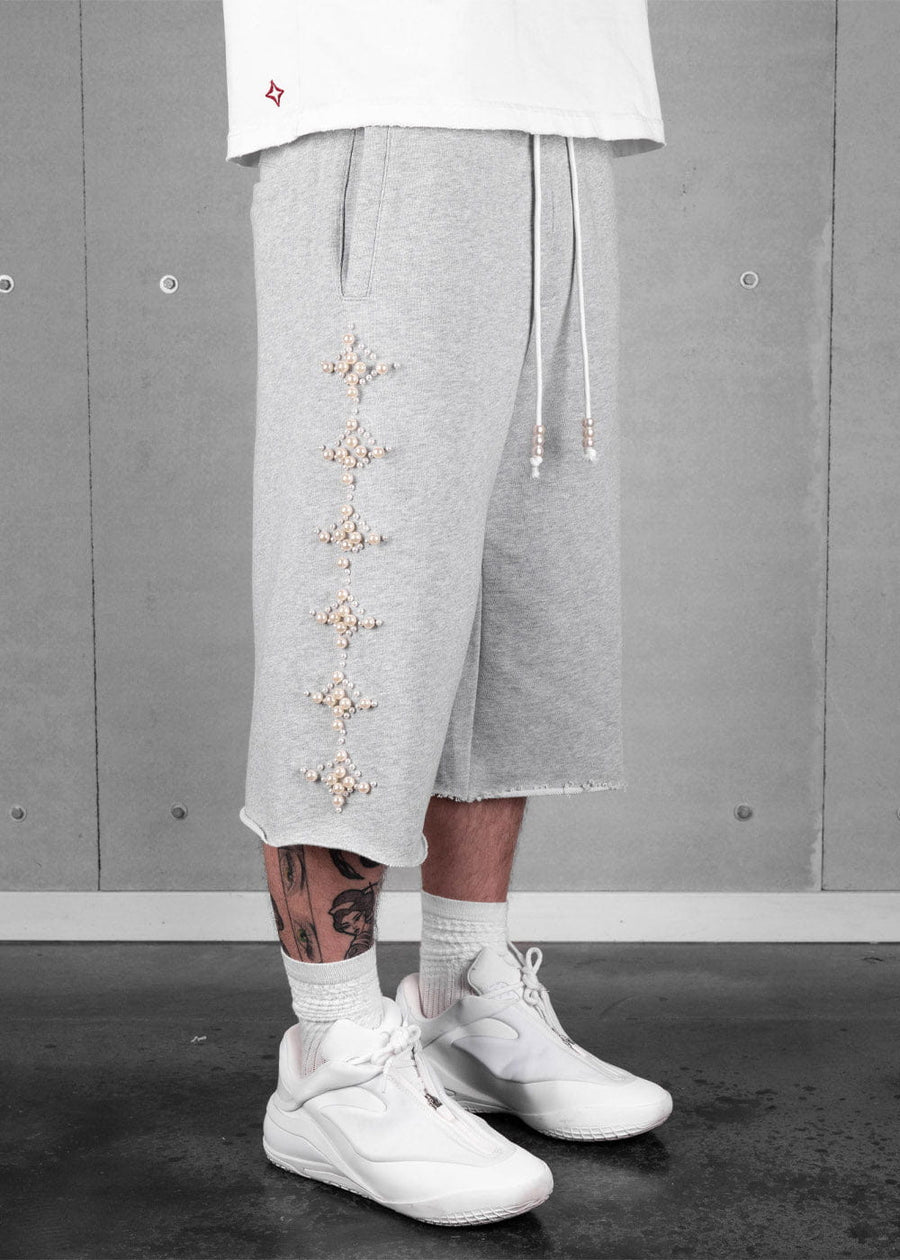 Model wearing heather gray long shorts with pearl-like star embellishments, beaded drawstrings, and raw hems.
