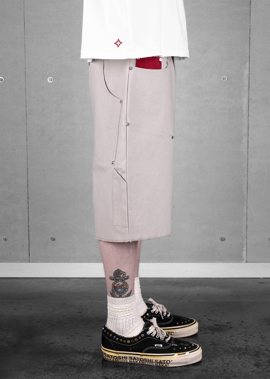 Side view of a model wearing light gray canvas shorts with metal rivets, a white T-shirt, white socks, and black sneakers.