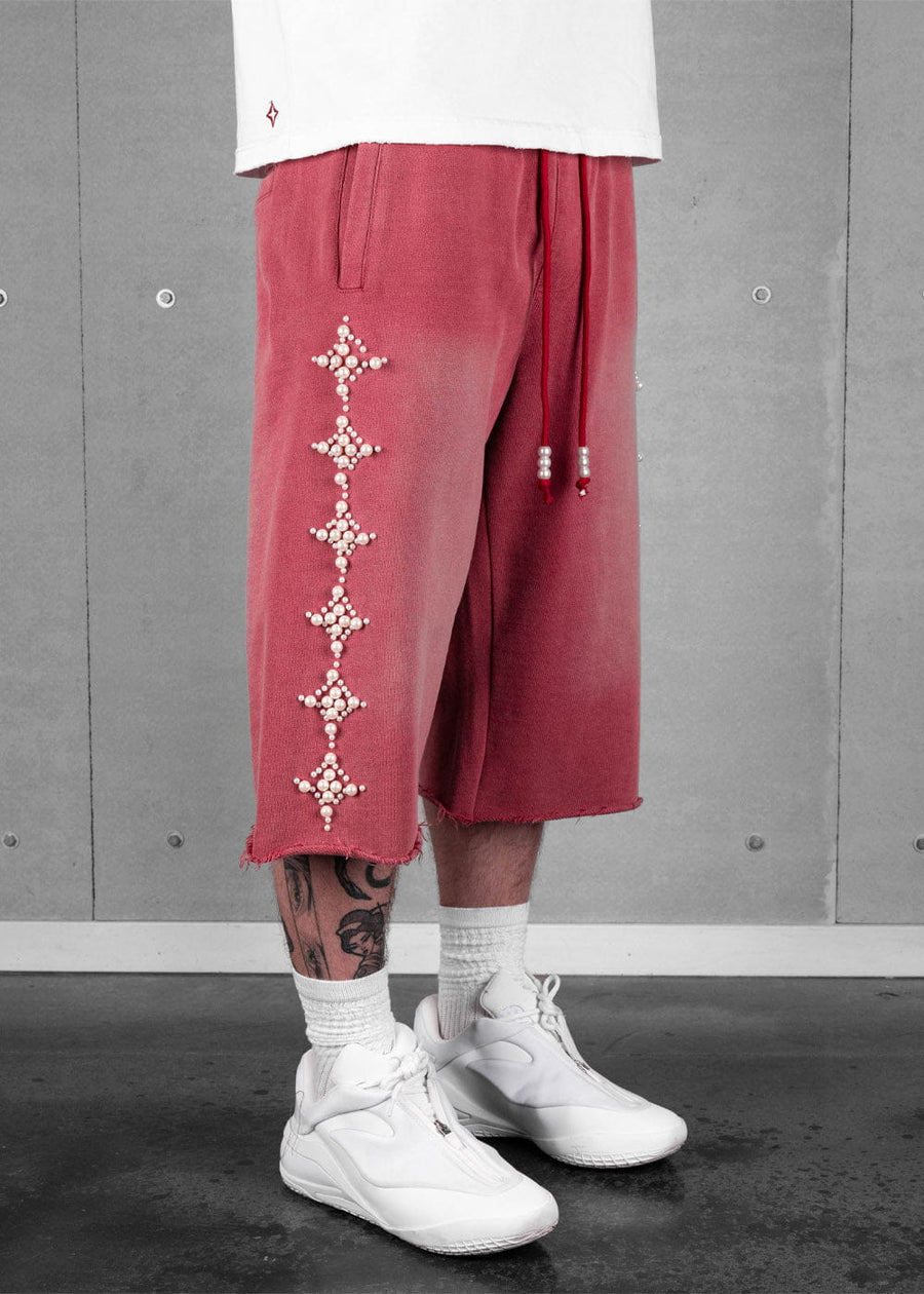 Model wearing faded red knit shorts with pearl-like star embellishments, beaded drawstrings, and raw hems.
