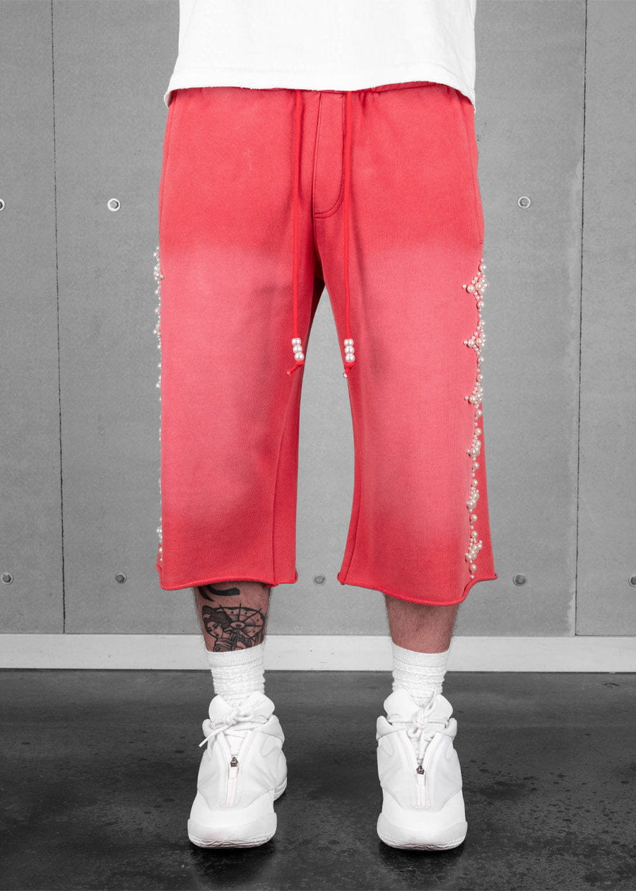 Model wearing coral red cropped sweatpants with pearl-beaded sides and drawstrings, white socks, and white sneakers.