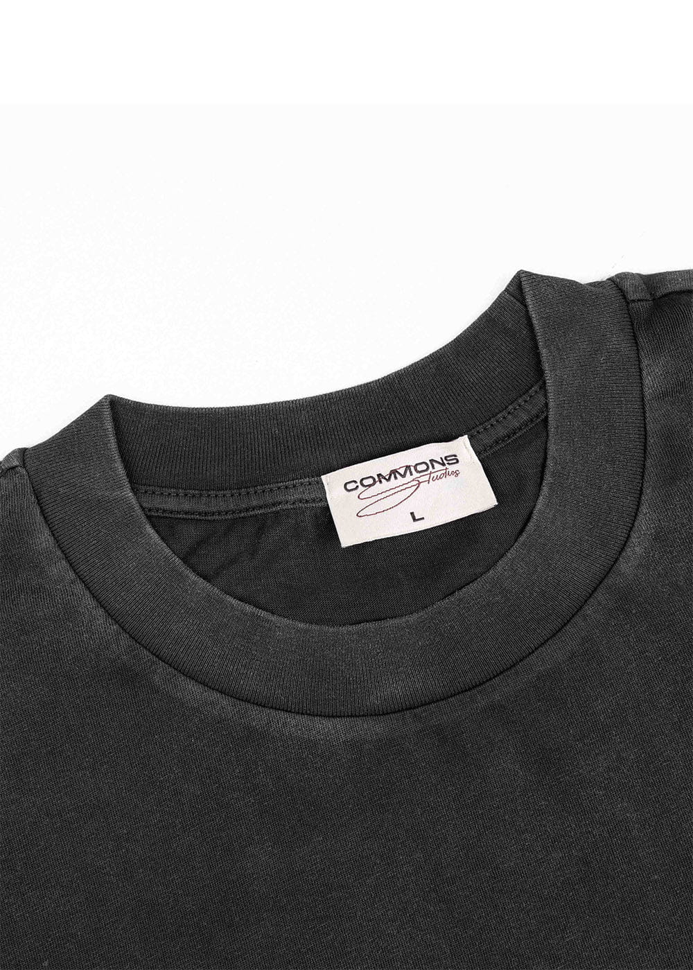 Close-up of a black T-shirt with a ribbed crew neck and white Commons Studios size L label on a white background.
