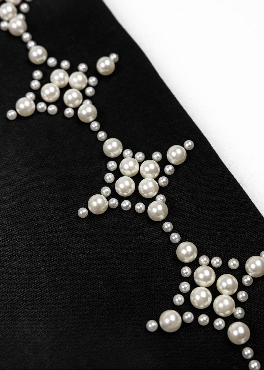 Close-up of black knit fabric with ivory pearl beads in geometric clusters on a white background.