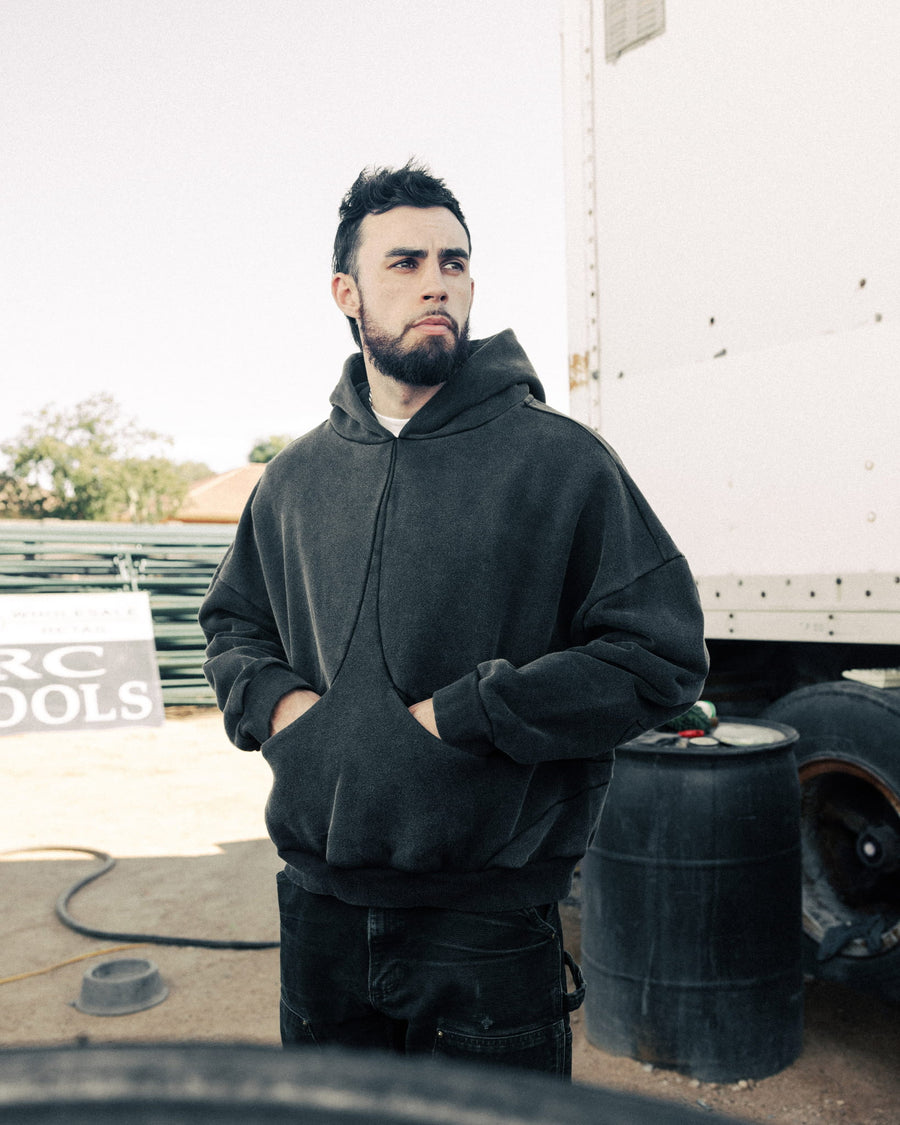 Man wearing an oversized charcoal pullover hoodie with a kangaroo pocket, standing outdoors beside a truck.