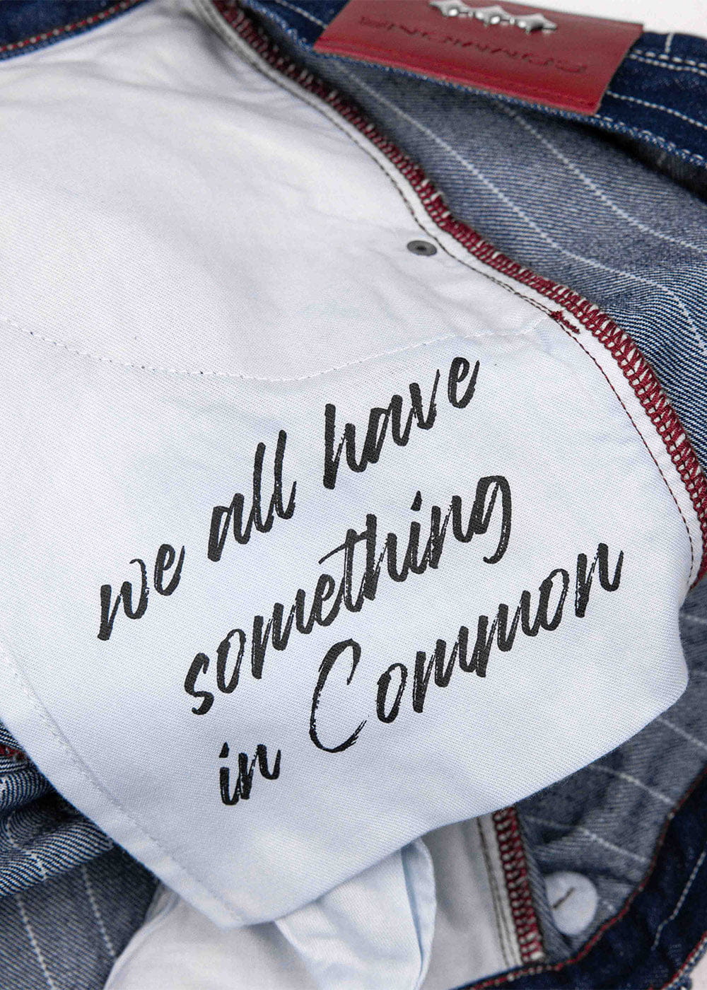 Blue denim jeans interior with white pocket lining, black script lettering, red stitching, and a red waistband label.