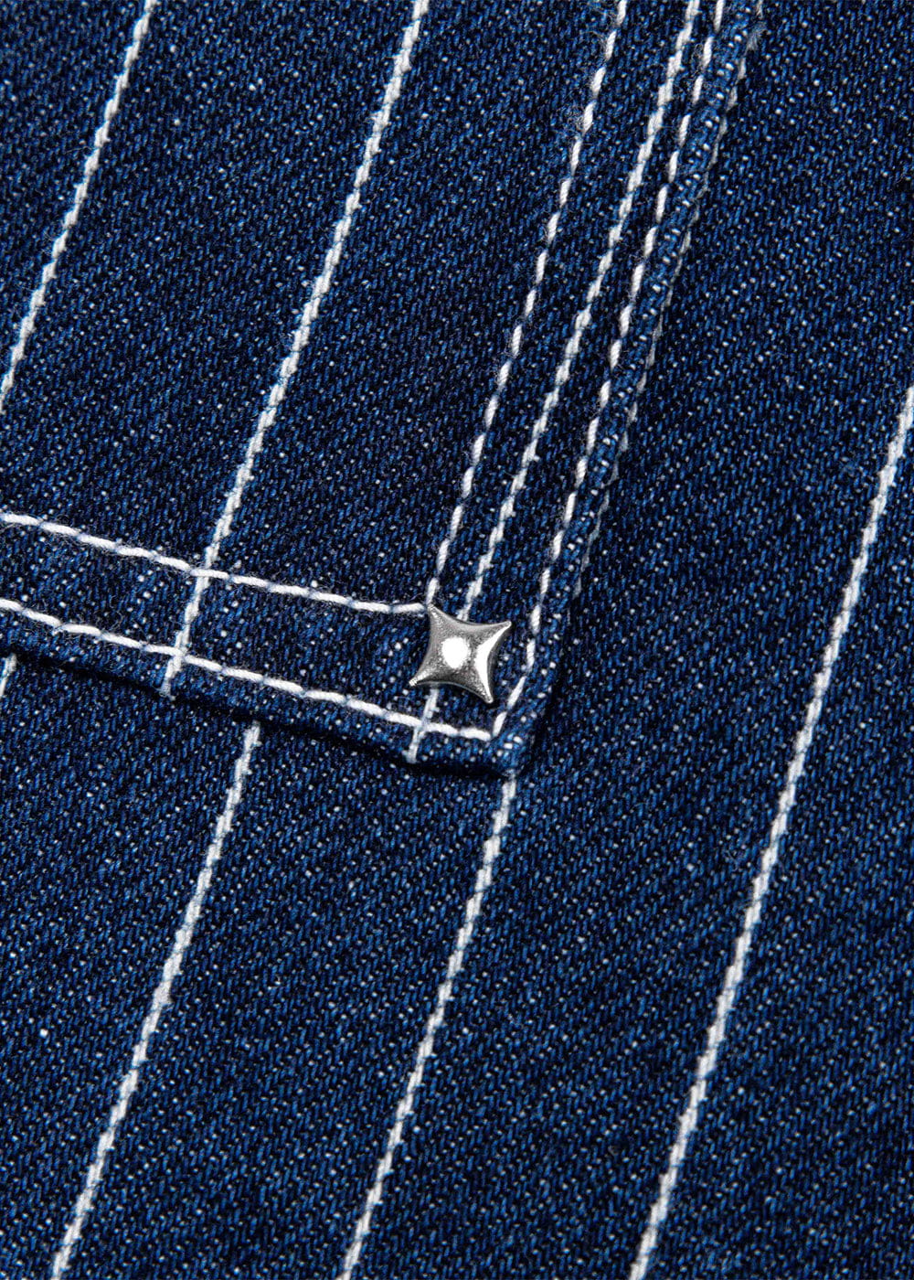 Close-up of dark blue denim with white pinstripes, a stitched pocket corner, and a silver star-shaped rivet.