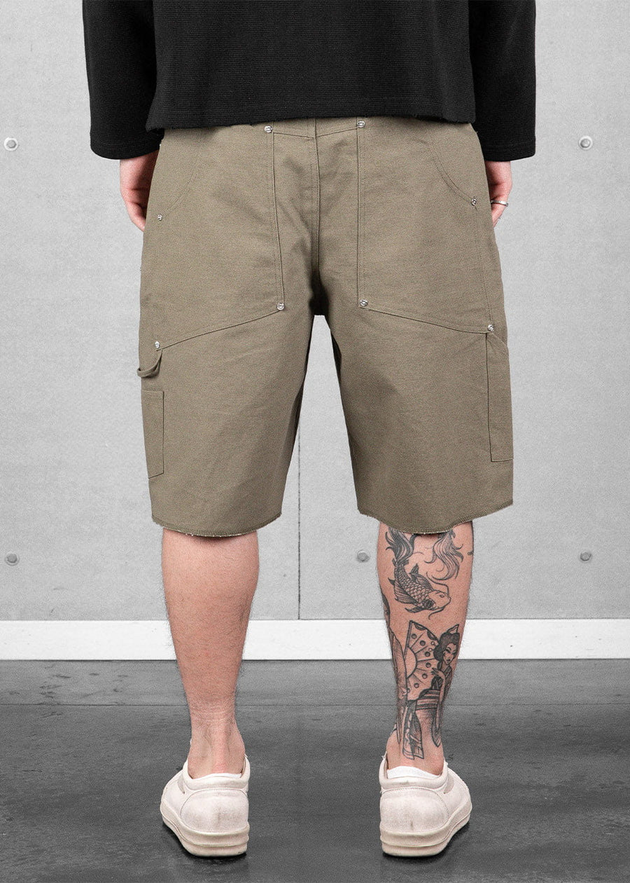 Rear view of olive green canvas shorts with riveted pockets and a hammer loop, worn with a black top and white sneakers.