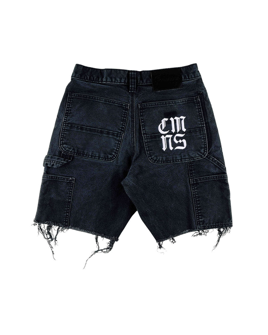 Back view of black denim carpenter shorts with frayed hems, utility pockets, and white lettering on one back pocket.