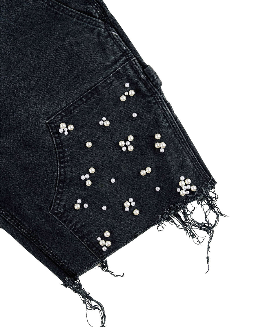 Close-up of black denim shorts with pearl-beaded pocket and frayed hem on a white background.