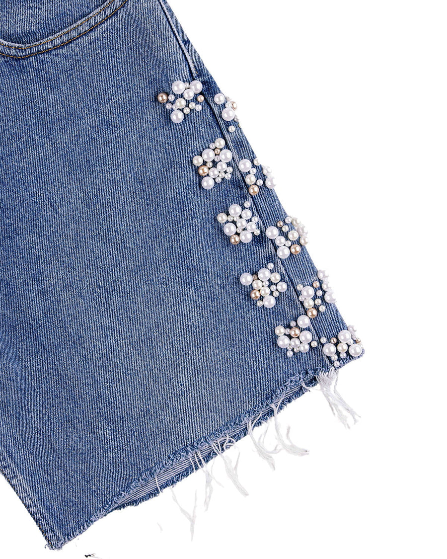 Close-up of blue denim shorts with white and gold pearl-like bead clusters along the side and a frayed hem.